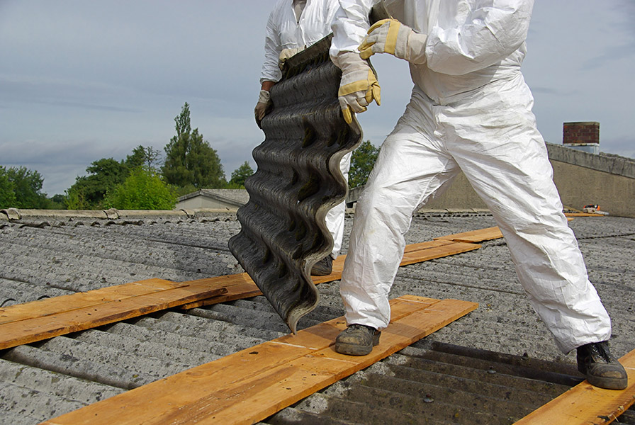 Dos trabajadores desmontando un tejado de uralita bien equipados para no contraer enfermedad profesional